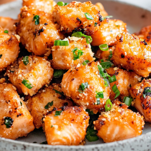 Crispy honey garlic salmon bites in a speckled ceramic bowl, garnished with chopped green onions.