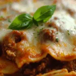 Closeup of cheesy Crockpot Ravioli Lasagna with melted mozzarella, meat sauce, and fresh basil garnish
